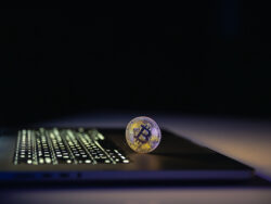 Bitcoin coin near laptop on black background. Finance and crypto money concept.