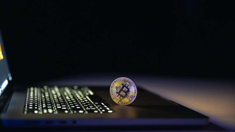 Bitcoin coin near laptop on black background. Finance and crypto money concept.