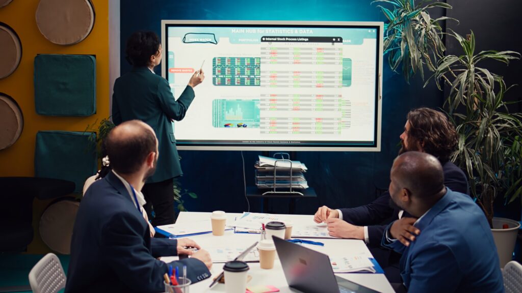 Operations manager develops sales strategies and targets, task based on market dynamics and customer feedback shown on interactive board. Specialist attends a meeting with colleagues. Camera B.